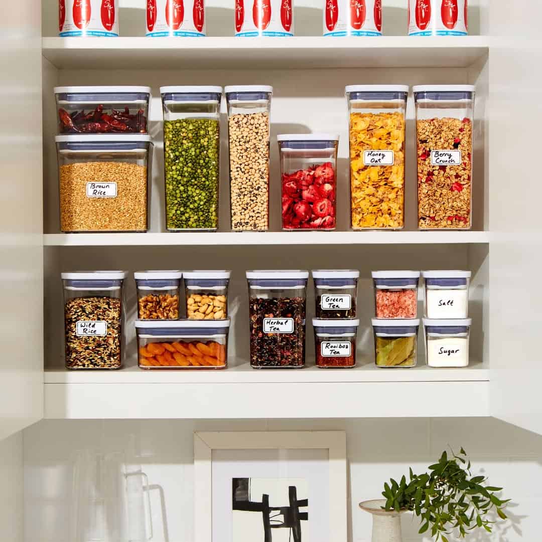 Clear containers of dried foods neatly organized on white shelves in a pantry, alongside essential cooking tools for beginners.