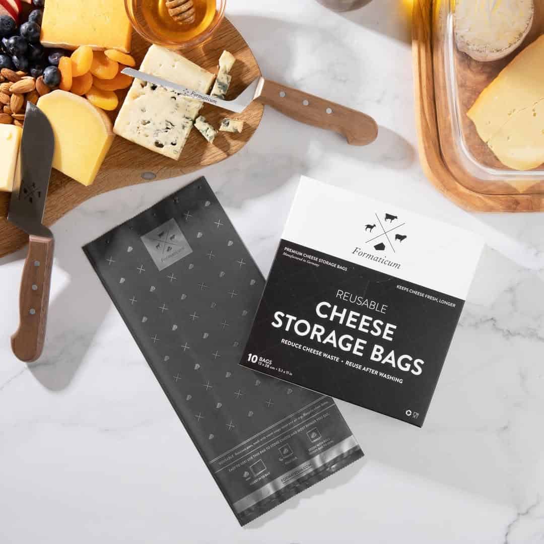Cheese storage bags and a cheese knife on a marble counter beside a cheese platter with assorted cheeses and fruit-perfect gifts for cheese lovers.