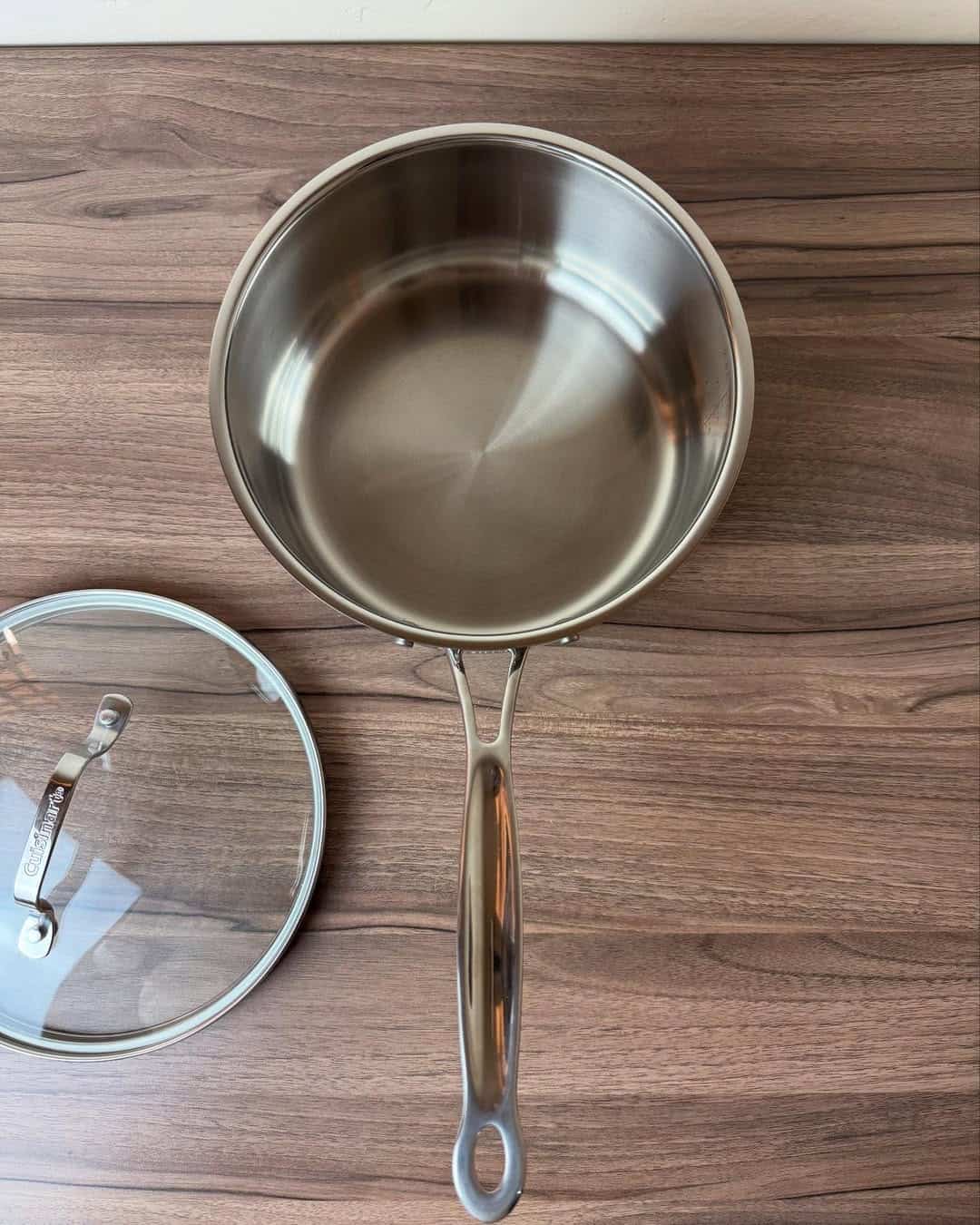 A stainless steel saucepan with a lid, one of the essential cooking tools for beginners, sits on a wooden surface.