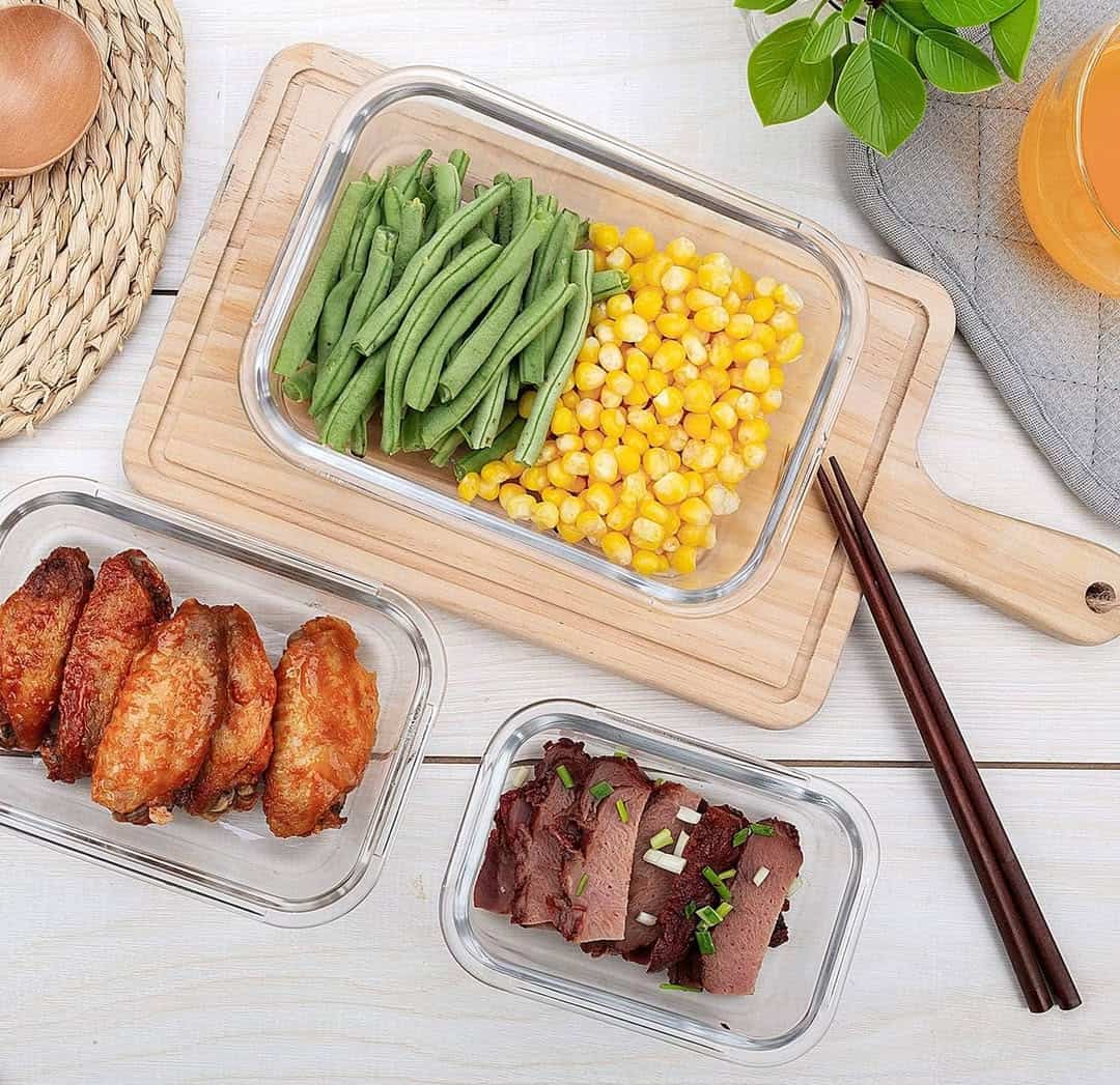 Three glass containers with green beans, corn, chicken wings, and sliced beef on a wooden cutting board.