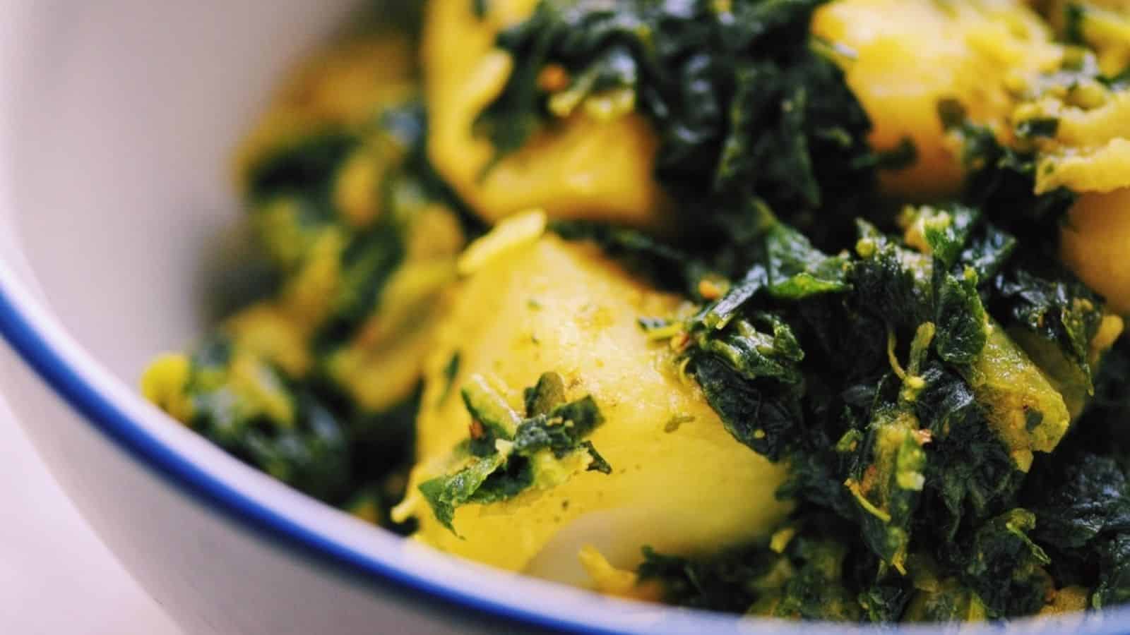 Close-up of cooked potatoes with chopped spinach and spices in a white bowl with a blue rim.