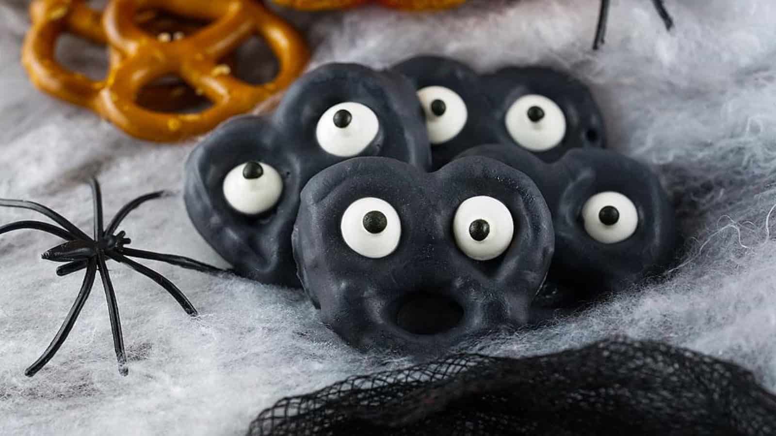 Black candy-coated pretzels with candy eyes arranged on spider-web decor.