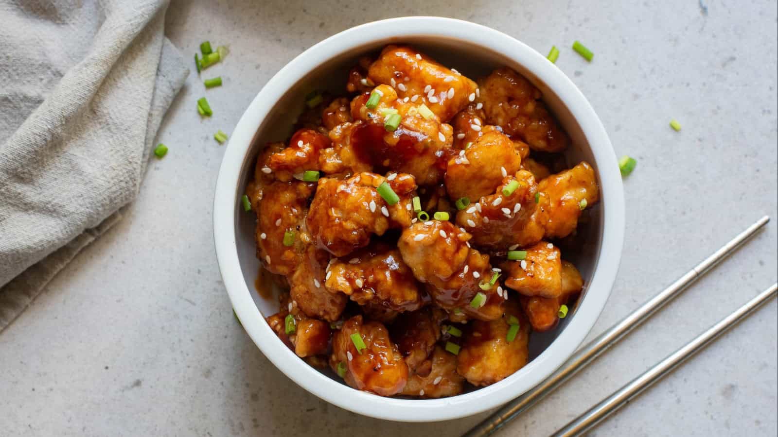 A bowl of asian chicken in a white bowl with chopsticks.