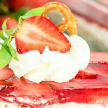 A slice of strawberry pretzel dessert topped with whipped cream, a strawberry, and a mini pretzel.