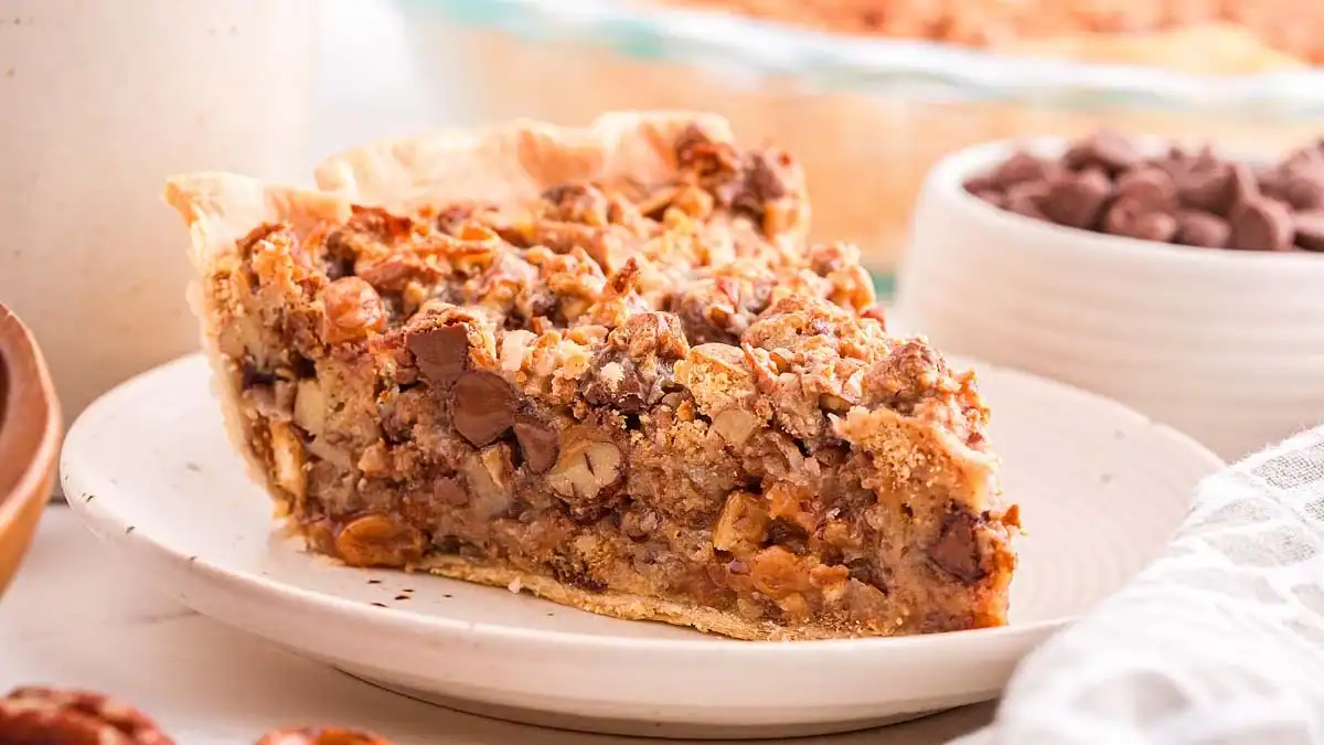 A slice of pie with a crumbly crust filled with pecans and chocolate chips on a white plate.