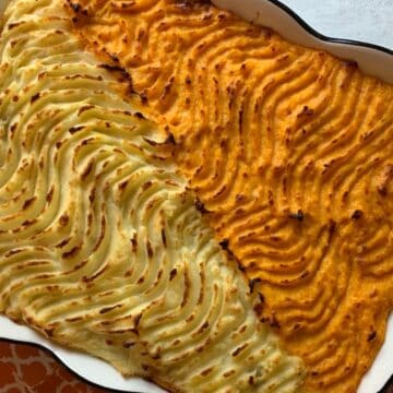 A baking dish with shepherd’s pie, half topped with white potatoes, half with orange sweet potatoes.