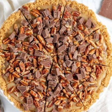Top view of a pie with chopped chocolate and pecans on top, sliced and placed on a white cloth.