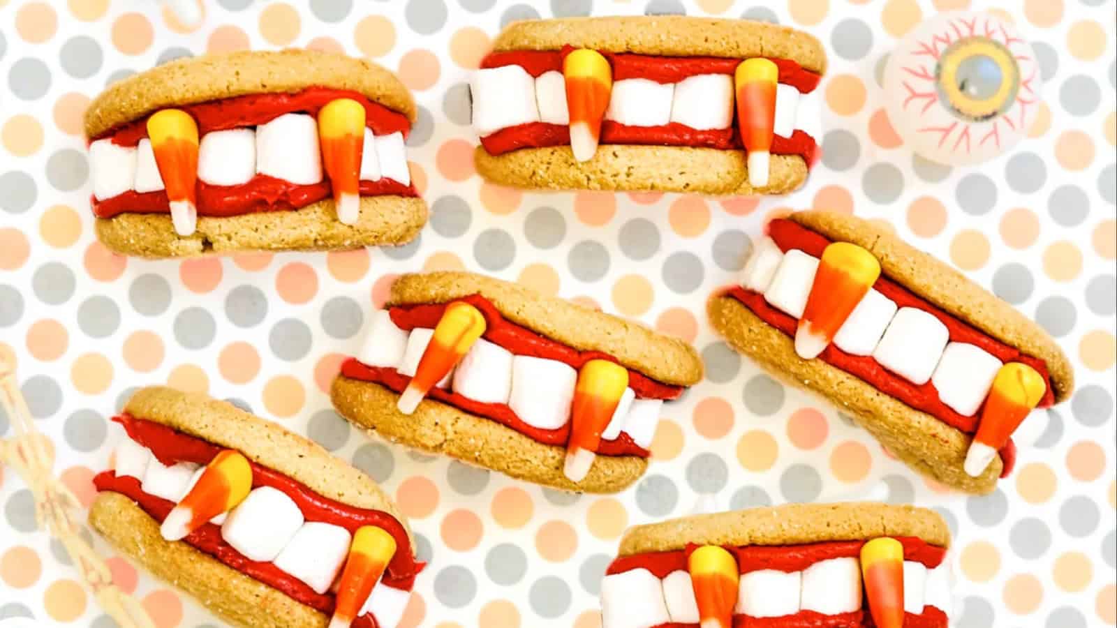 Five Halloween-themed cookie sandwiches resemble vampire mouths. The background features a polka dot pattern in pastel colors.