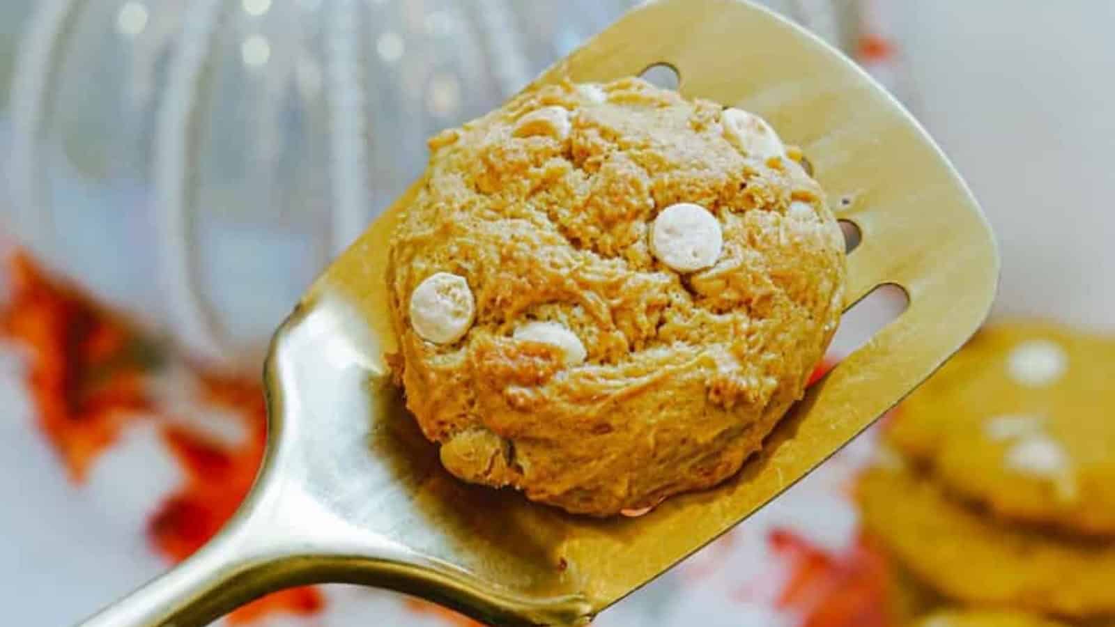 White cholate chip cookie on a spatula, with a plate of cookies in the background.
