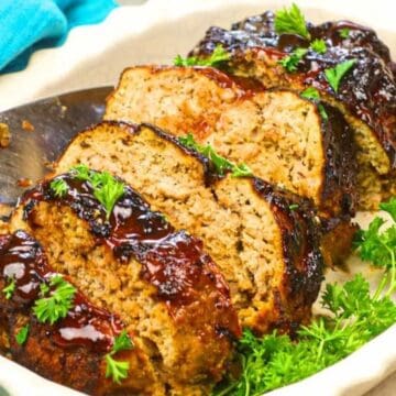 Sliced meatloaf with a glossy glaze, garnished with fresh parsley on a white serving dish.