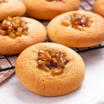 Round cookies with caramelized apple filling on a cooling rack, with a cup partially visible in the foreground.