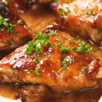 Glazed baked chicken thighs garnished with chopped parsley in a white casserole dish.