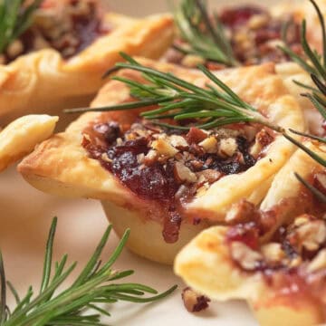 Mini puff pastry tarts filled with nuts and jam, garnished with fresh rosemary on a white plate.