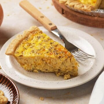 A slice of onion quiche on a plate with a fork, with a whole onion nearby on the table.