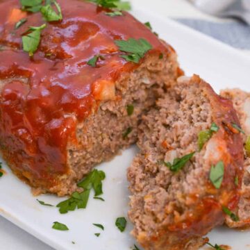 A sliced meatloaf topped with tomato sauce and chopped parsley on a white plate, garnished with fresh herbs.