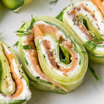 Cucumber rolls filled with cream cheese, smoked salmon, and fresh dill, garnished with black sesame seeds.