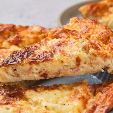 A slice of cheesy, golden-brown quiche being lifted from a plate with a serving spatula.