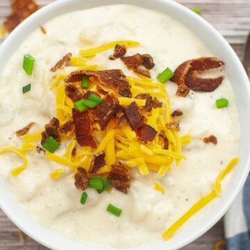 Bowl of creamy potato soup topped with shredded cheese, bacon bits, and chopped green onions.