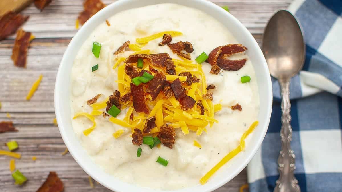 Bowl of creamy potato soup topped with shredded cheese, bacon bits, and chopped green onions.