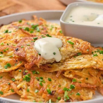 Crispy potato pancakes garnished with chives, topped with sour cream, served with a side of dipping sauce.
