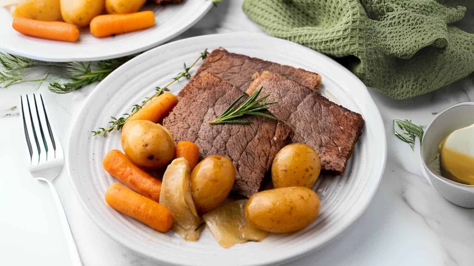 A plate with sliced rump roast, baby potatoes, carrots, and onions, garnished with a sprig of rosemary.