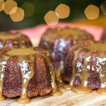 Four sticky toffee puddings with caramel sauce drizzled on top, arranged on a wooden board.