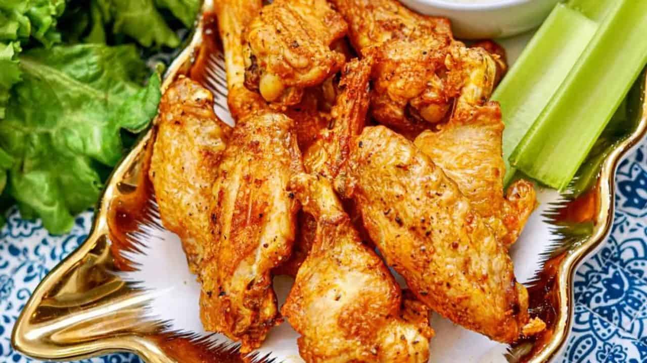 A plate of cooked chicken wings with celery sticks and a bowl of dipping sauce, garnished with leafy greens on the side.