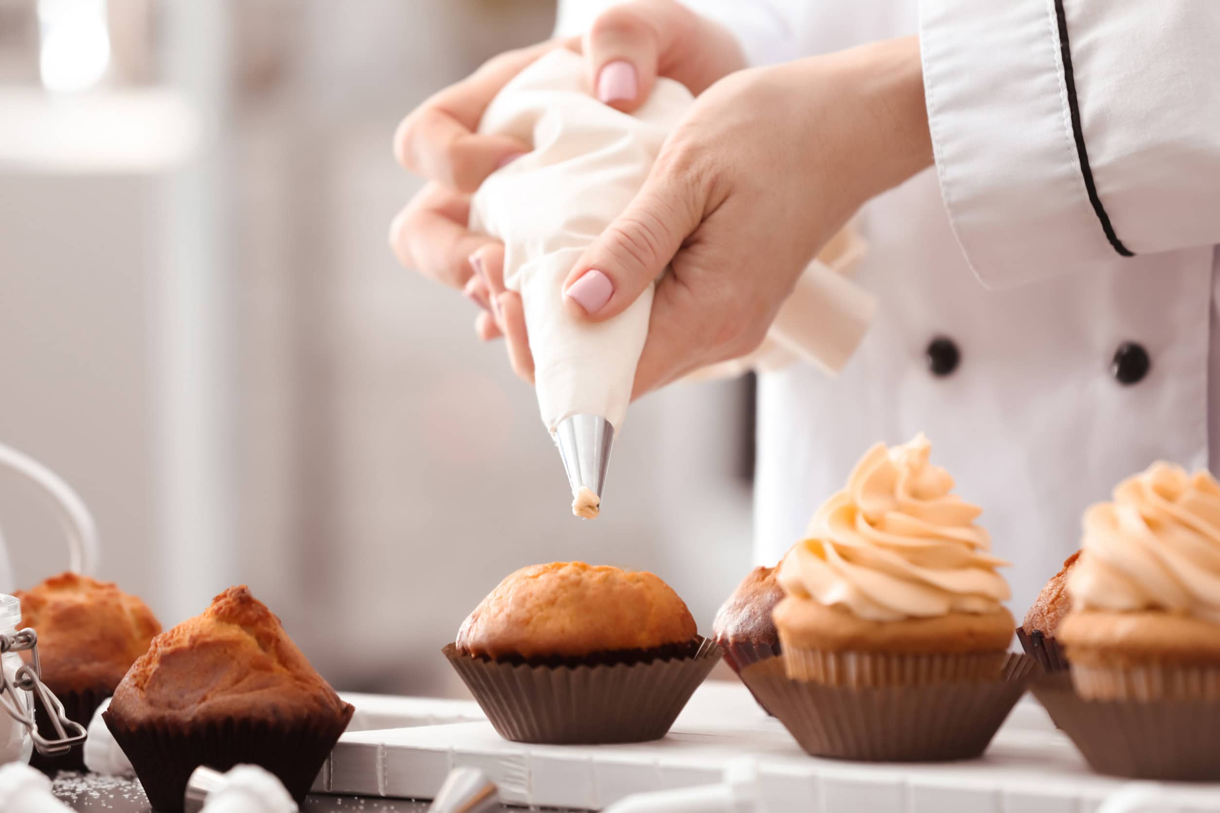 A baker piping frosting onto cupcakes with a pastry bag on a kitchen counter, showcasing essential kitchen tools for holiday baking.