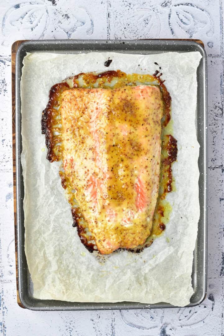 Baked salmon fillet with a golden honey mustard glaze on parchment paper in a baking tray.