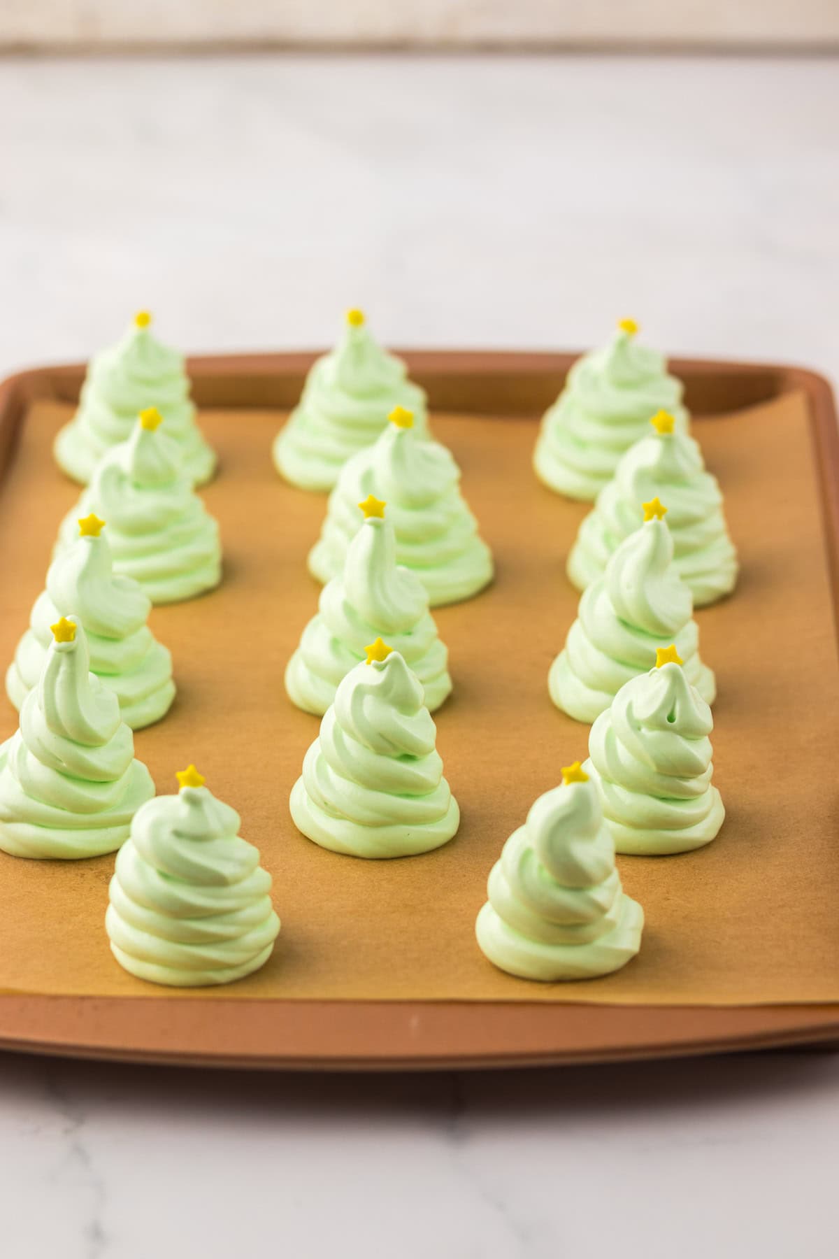 Green meringue cookies shaped like Christmas trees with yellow star decorations on a baking sheet.