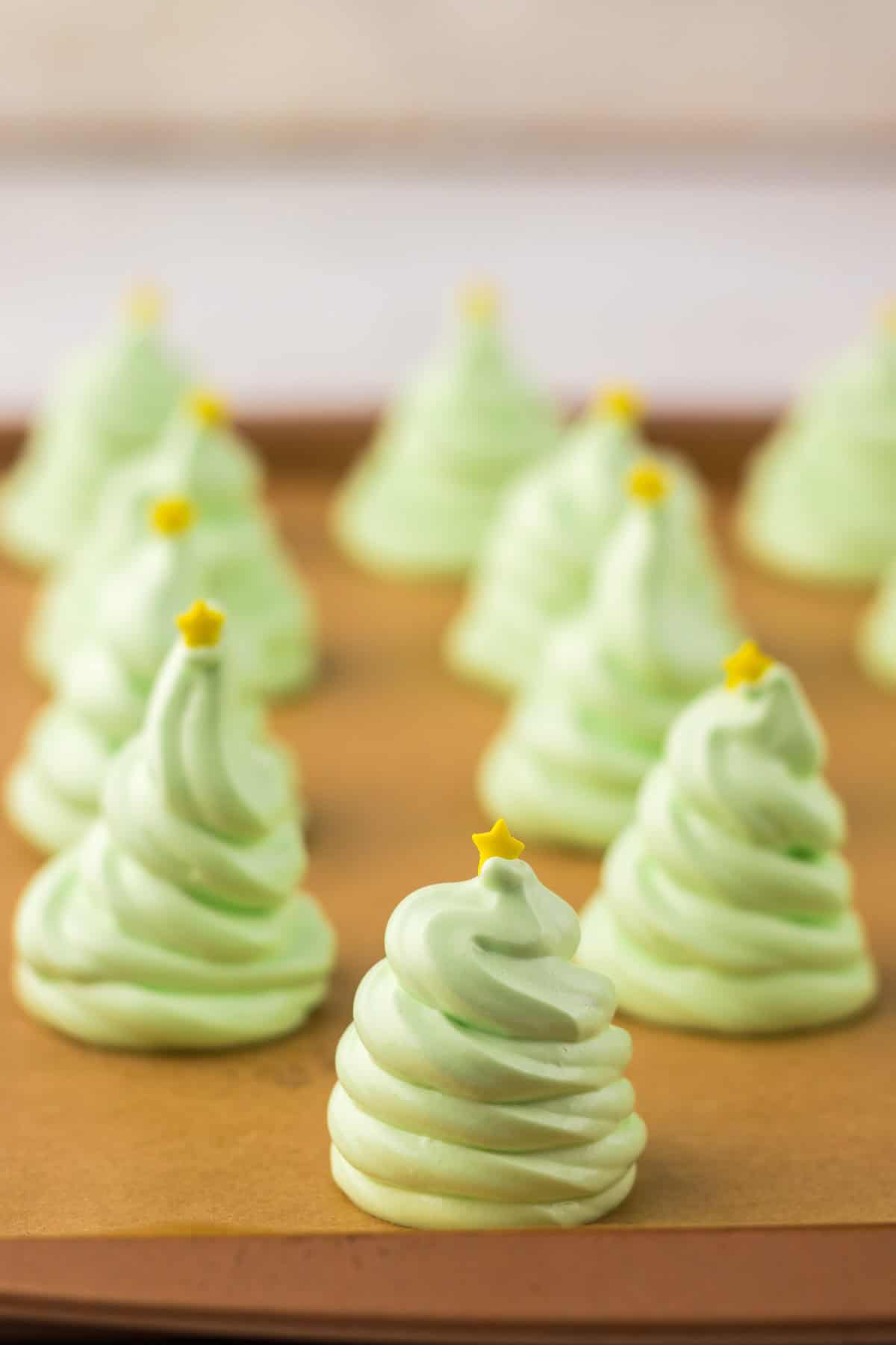 Green meringue cookies shaped like Christmas trees with yellow star toppers on a brown surface.