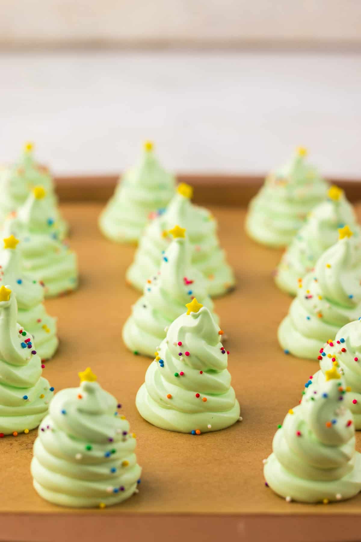 Green meringue cookies shaped like Christmas trees with sprinkles and star toppers on brown parchment paper.