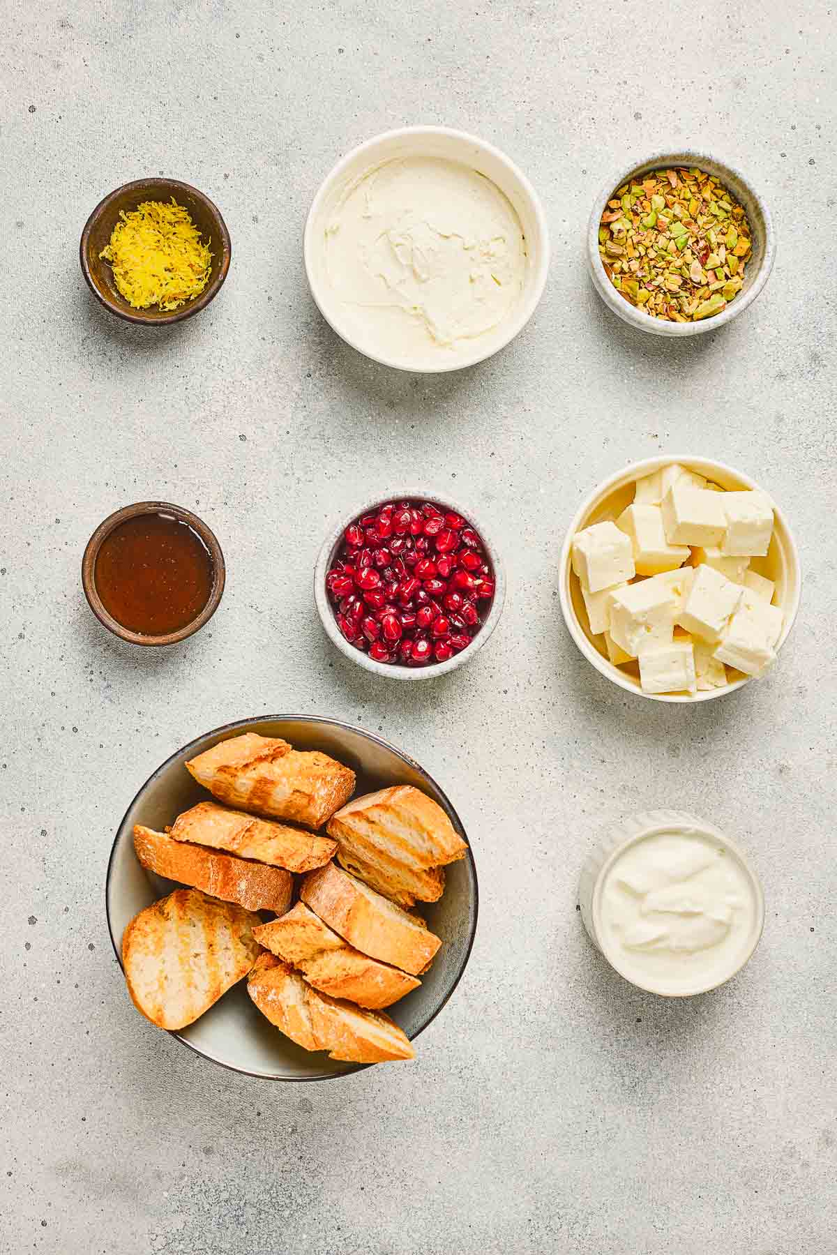 Bowls of grilled bread, feta, yogurt, pomegranate seeds, honey, pistachios, lemon zest, and a creamy spread.