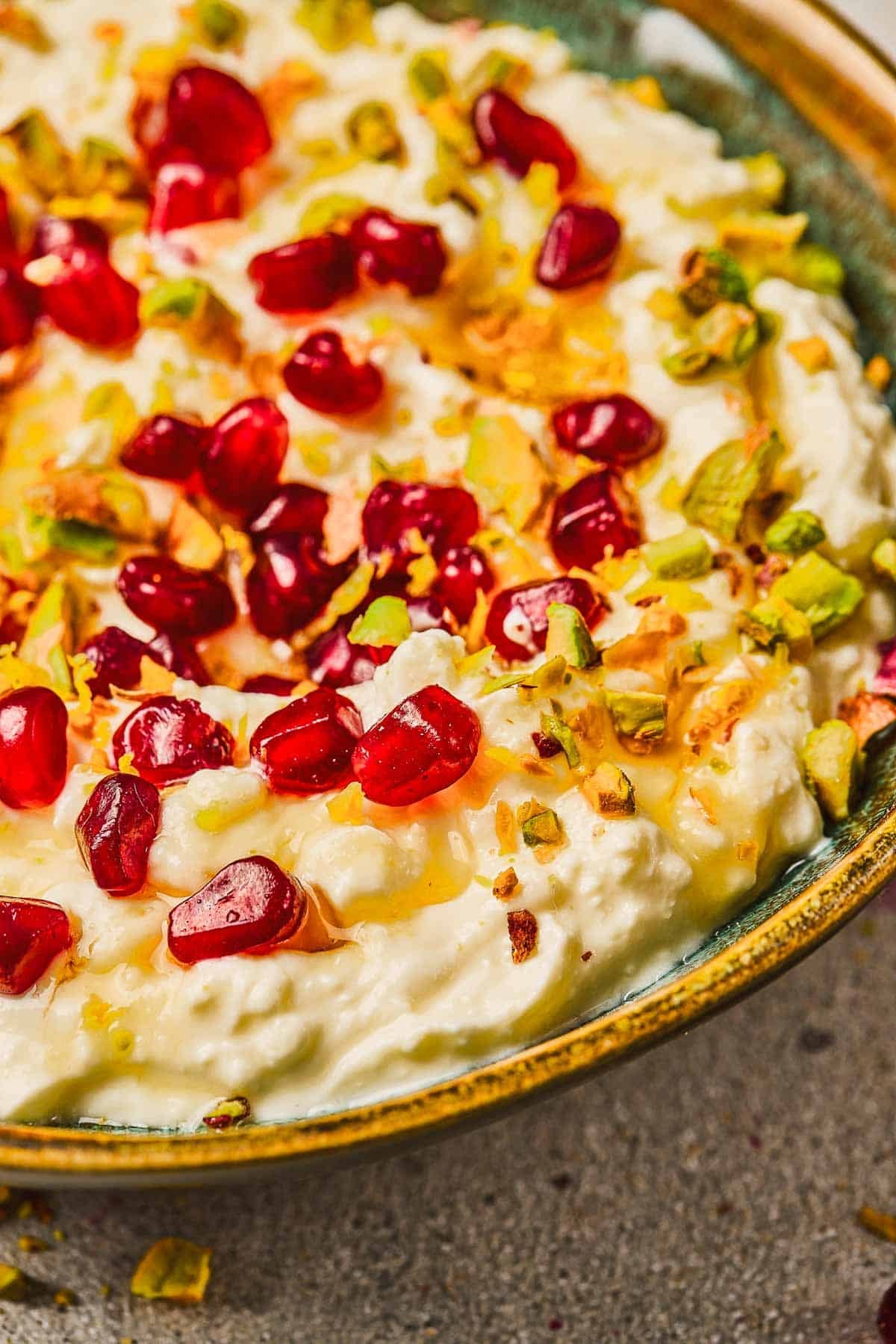 Pomegranate Pistachio Whipped Feta&mdash;a creamy dip topped with pomegranate seeds, chopped pistachios, and a drizzle of honey in a ceramic bowl.