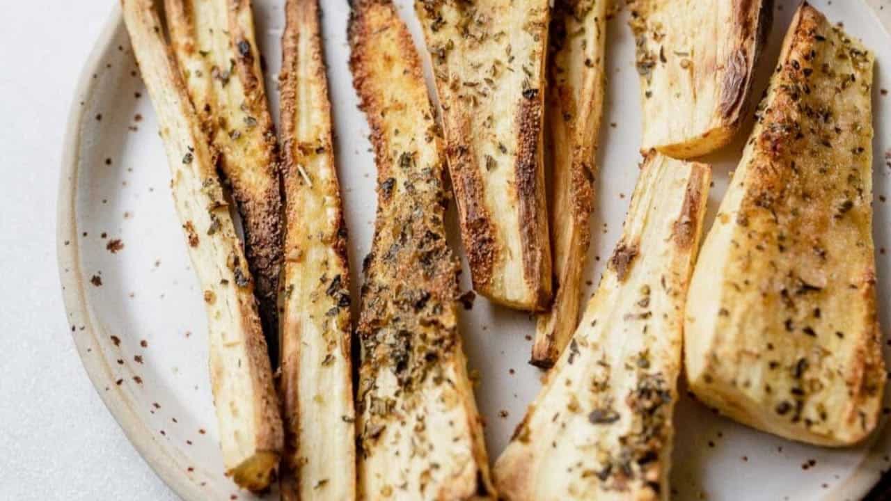 Oven-roasted parsnip wedges with herbs and seasoning on a white plate.