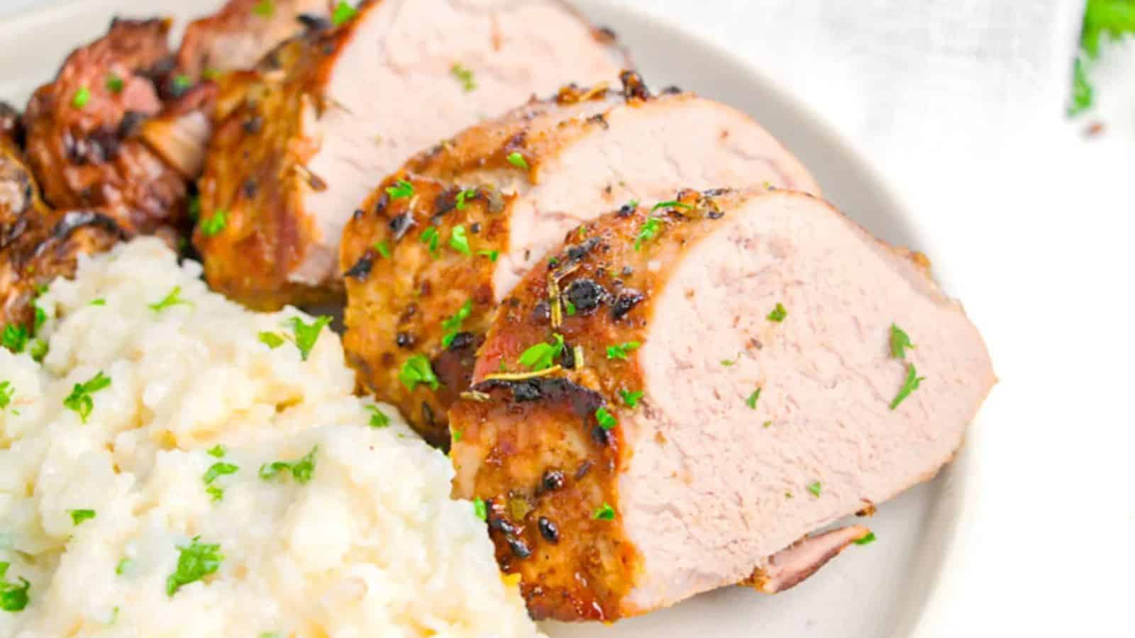 Sliced roasted pork tenderloin with herbs served on a plate next to mashed potatoes—perfect for those seeking budget dinners without sacrificing flavor.