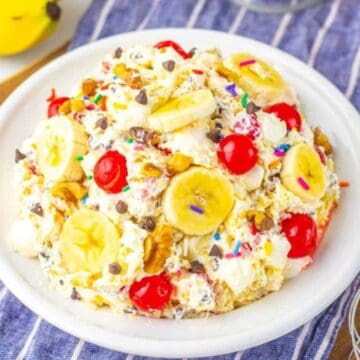 A bowl of banana split salad with bananas, cherries, walnuts, chocolate chips, and sprinkles on top.