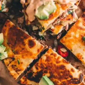 Golden, crispy quesadillas topped with avocado and sliced red chili peppers on parchment paper.