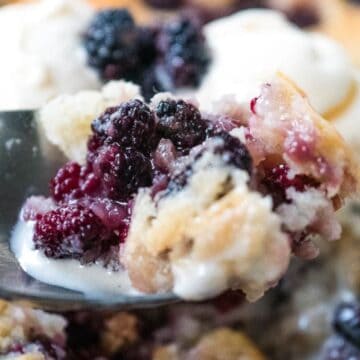 A spoonful of berry cobbler with vanilla ice cream, showing juicy berries and golden crust.