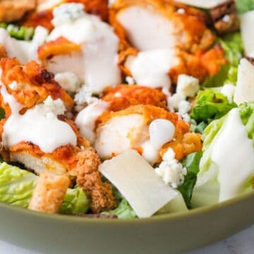 A bowl of salad with crispy chicken, lettuce, croutons, cheese, and creamy dressing.