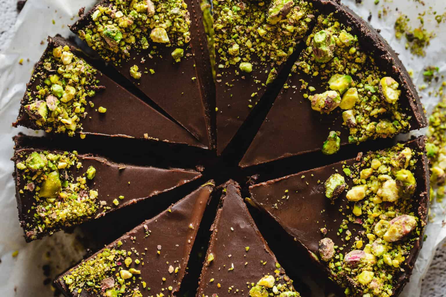 Chocolate tart topped with crushed pistachios, sliced into several pieces on parchment paper.