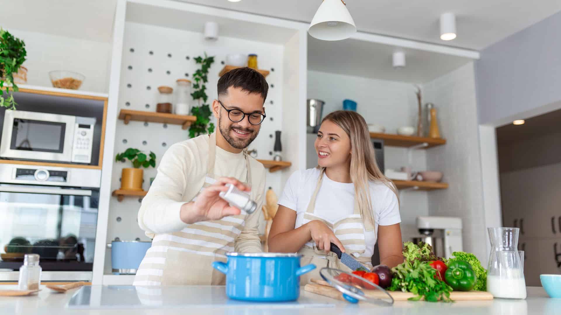 Smiling couple cooking together in a modern kitchen with fresh vegetables and handy kitchen gadgets for holiday cooking on the counter.