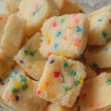 A bowl of square vanilla cookies with colorful sprinkles on top.