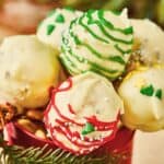 Christmas Cake Pops made with white chocolate are decorated in red, green, and yellow icing, arranged beautifully in a festive container.