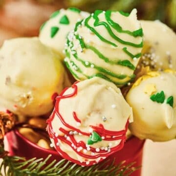 Christmas Cake Pops made with white chocolate are decorated in red, green, and yellow icing, arranged beautifully in a festive container.
