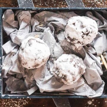 Three powdered sugar-coated chocolate cookies in a gift box lined with crumpled tissue paper.