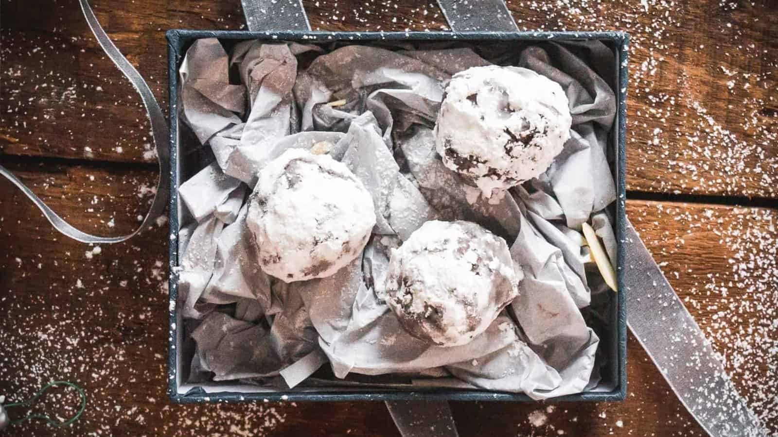 Three powdered sugar-coated chocolate cookies in a gift box lined with crumpled tissue paper.