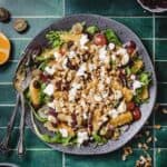 Arugula salad with orange slices, grapes, walnuts, cranberries, and goat cheese on a gray plate.
