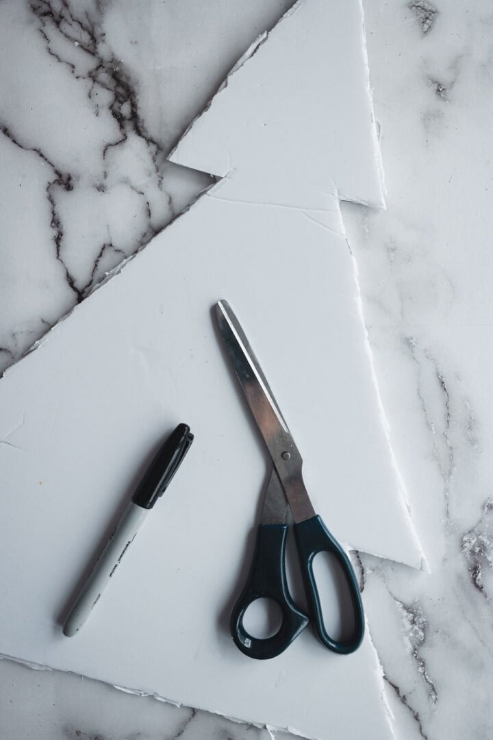 A black marker and scissors on a marble surface next to a cut-out foam sheet shaped like a Christmas Tree Charcuterie Board.