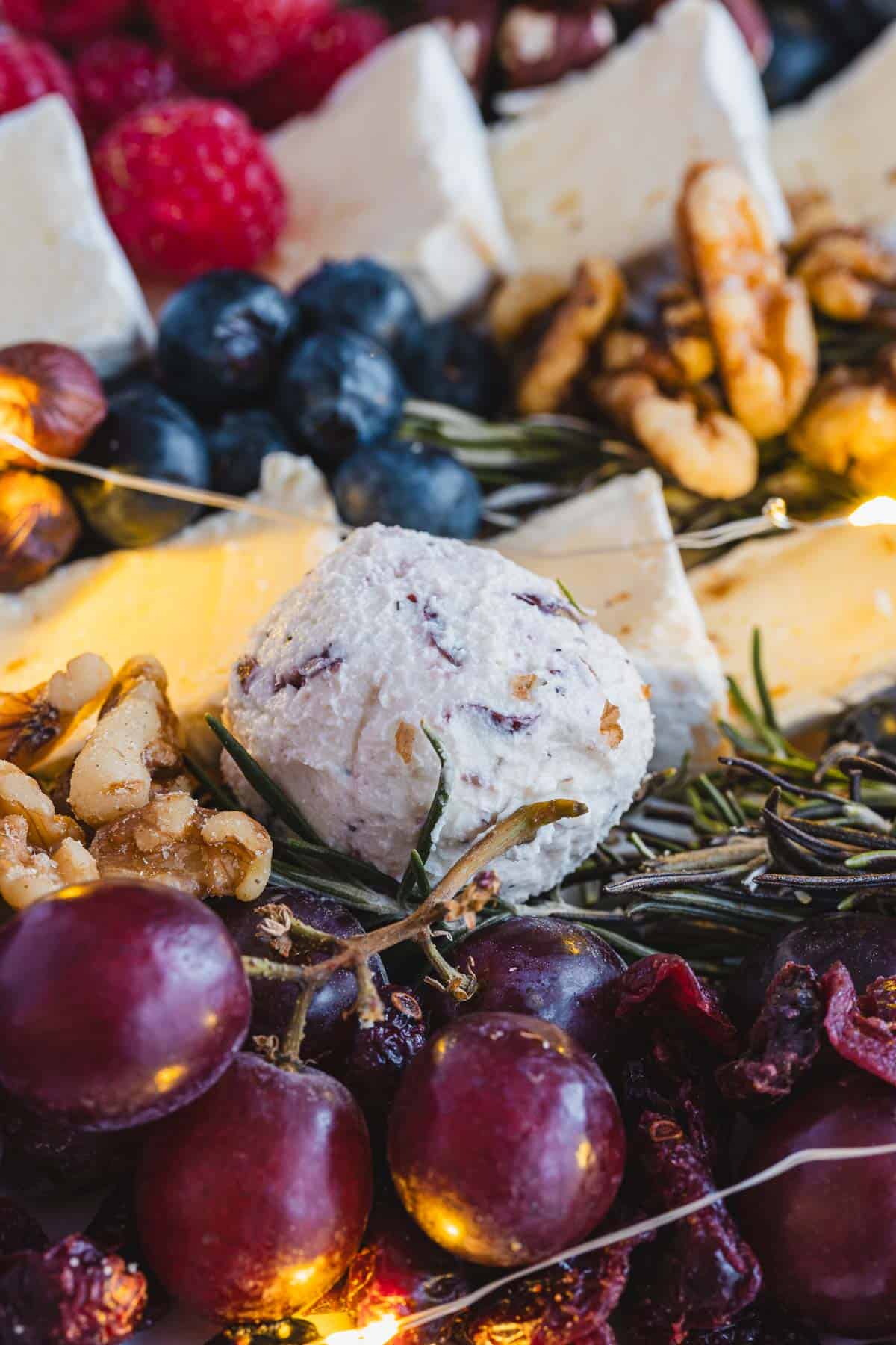 Close-up of grapes, blueberries, brie cheese, walnuts, and a cheese ball arranged on a festive Christmas Tree Charcuterie Board.